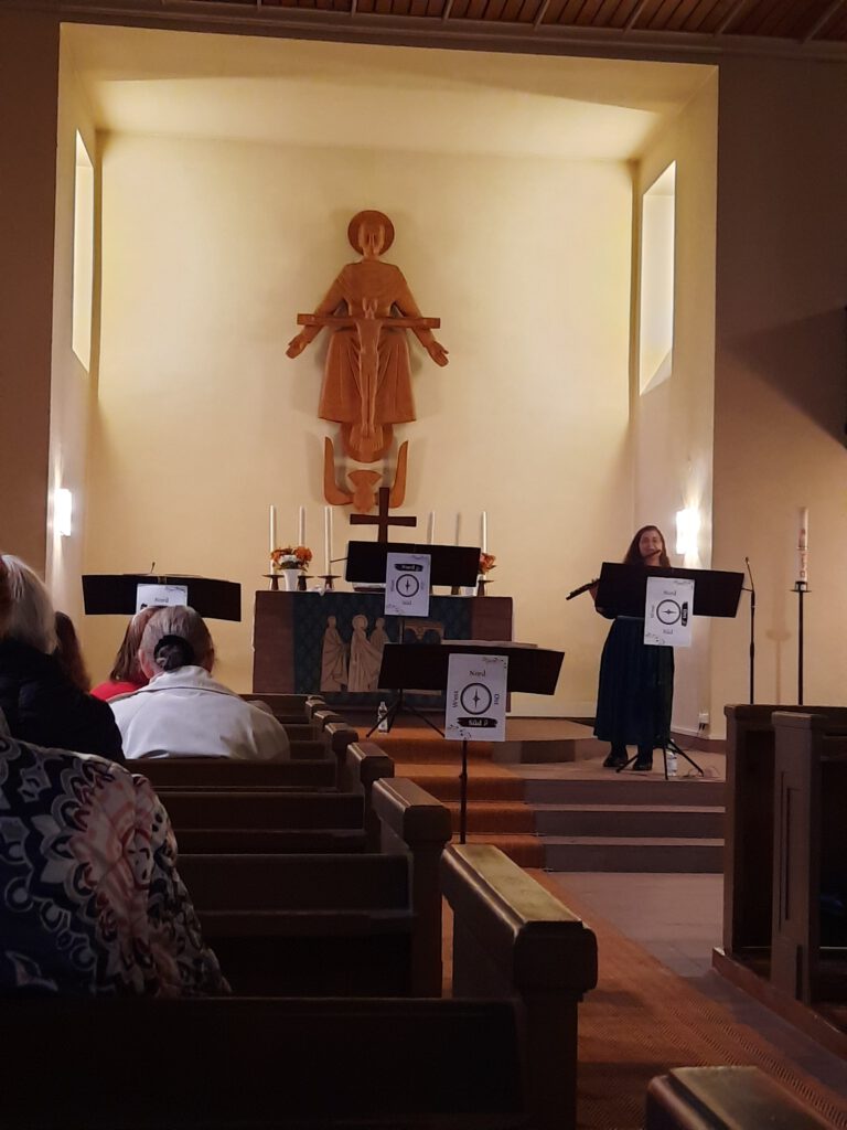 Flötensplitter - das interaktive Konzert am 23.10.2022 in der Dreifaltigkeitskirche DA-Eberstadt Ute-Gabriela Schneppat mit Flöte am Notenständer mit der Himmelsrichtung Ost, Blick aus dem Publikum auf den Altarraum mit allen vier Notenständern