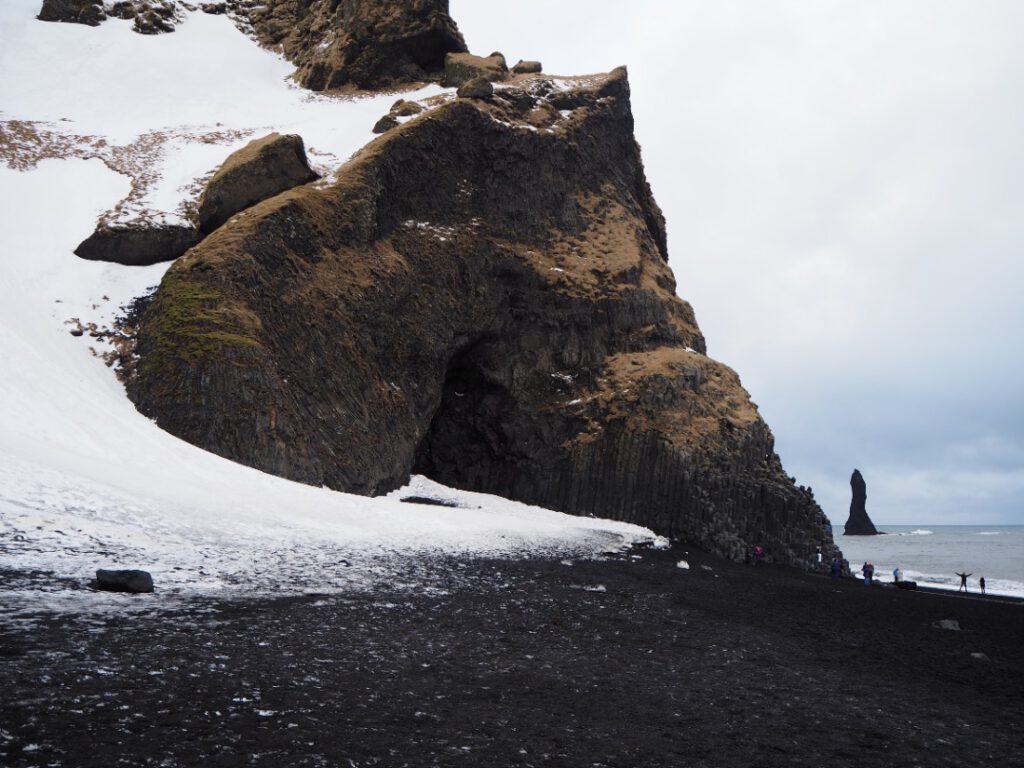 Der schwarze Strand Reynisfjara mit den Basaltsäulen. Im Hintergrund ein Felsen der versteinerten Trolle