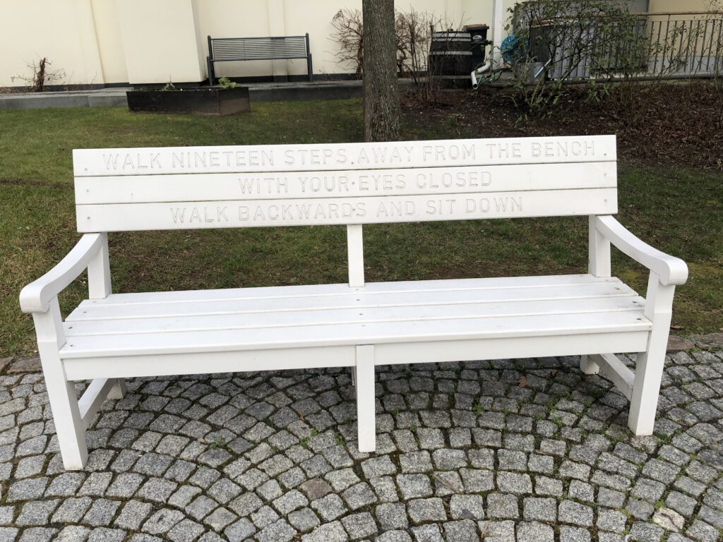 weiße Bank im Hof des Sinclair-Hauses mit der Beschriftung: Walk nineteen steps away from the bench with your eyes closed walk backwards and sit down